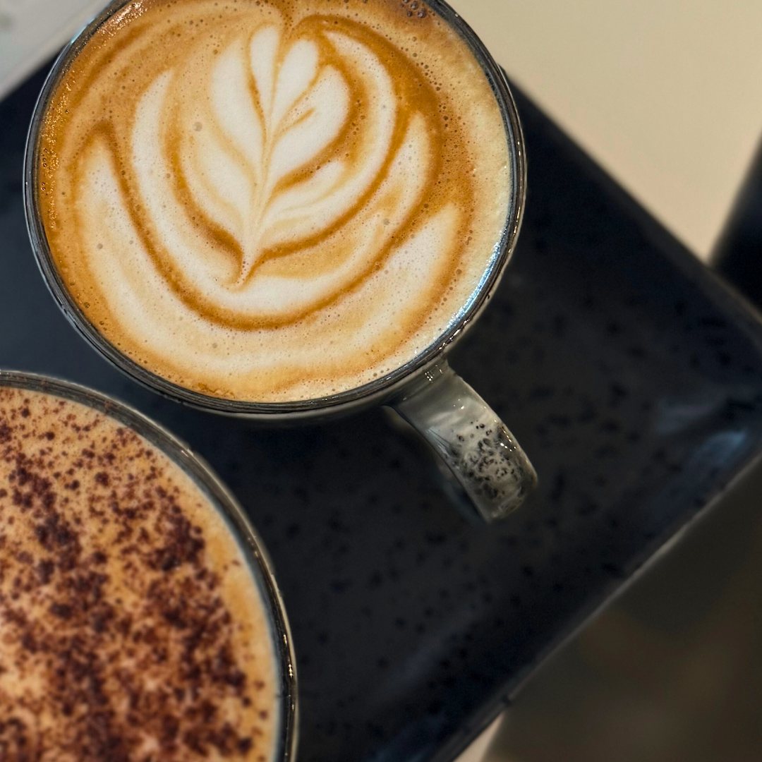 Two coffees seen from above: a latte with a leaf of latte art and a cappuccino dusted with chocolate