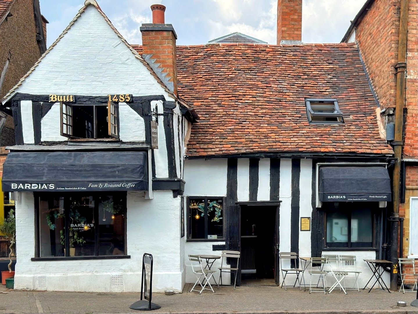Bardia's on Sheep Street: a white timber-framed house with black beams, "Built 1485" in gold letters on the beam, a black awning reading "Bardia's, Artisan Sandwiches & Cakes, Family Roasted Coffee", and tables outside